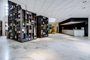 Un vestíbulo espacioso con diseño moderno, que presenta una zona central amplia con una recepción, rodeada de altas estanterías llenas de libros y plantas.