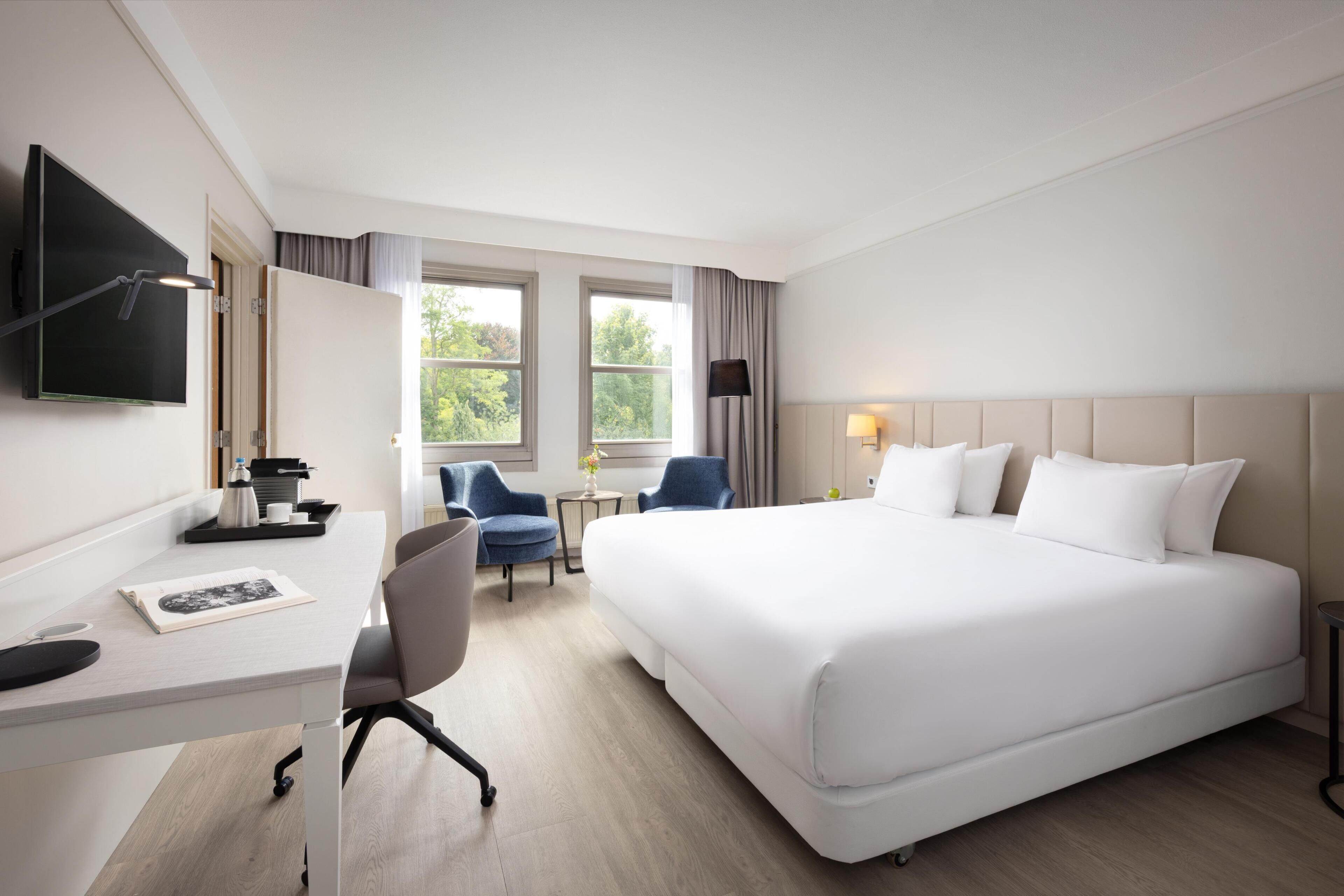 Ein Hotelzimmer mit Bett, Schreibtisch, Stuhl, Fernseher und Fenstern.