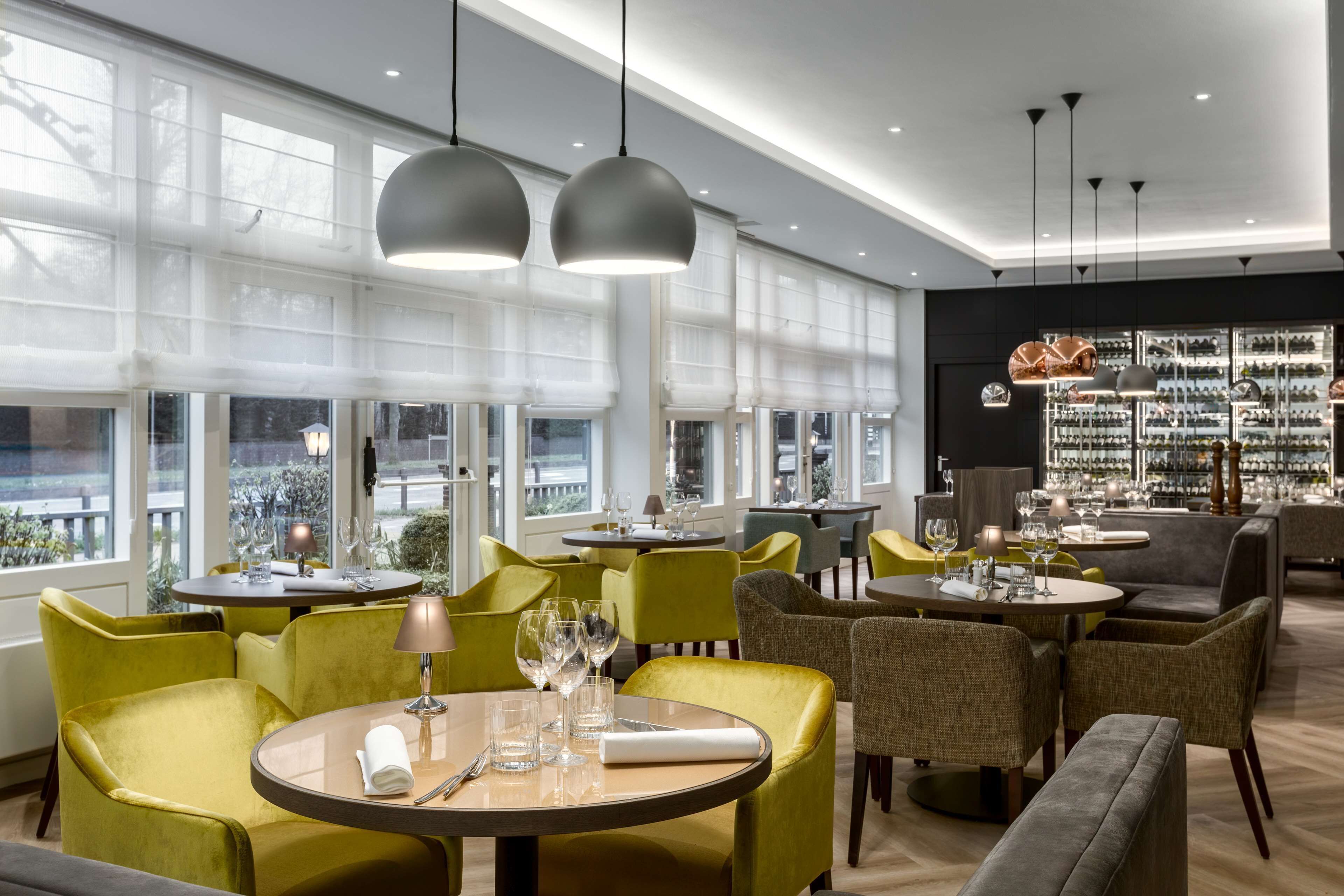 Un restaurante moderno con mesas redondas, sillas verdes y grises, e iluminación colgante.