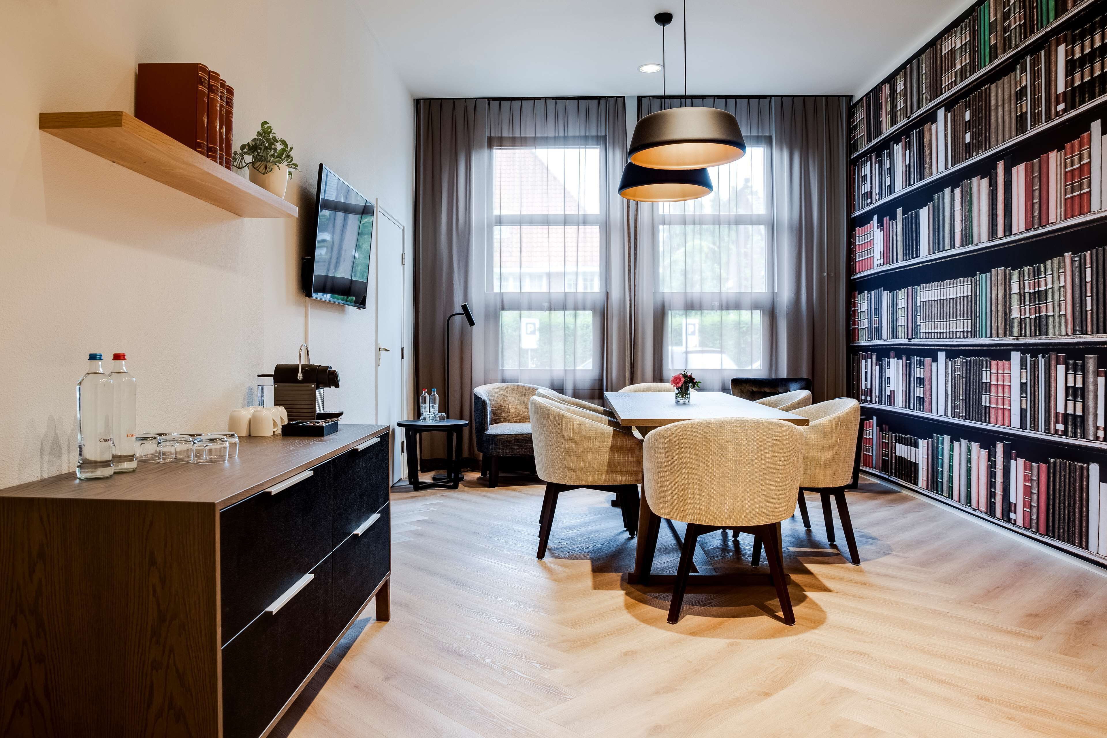 A modern library with a wooden desk, chairs, a bookshelf, and a television on the wall.