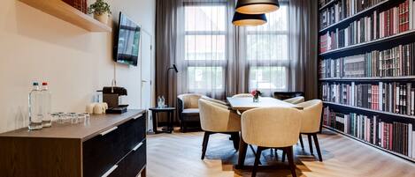 A modern library with a wooden desk, chairs, a bookshelf, and a television on the wall.