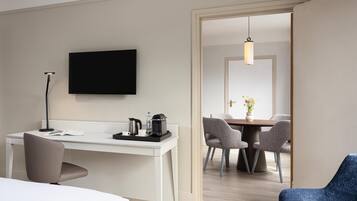Habitación de hotel con escritorio, silla, televisor de pantalla plana, mesita de noche y zona de comedor con sillas y mesa.