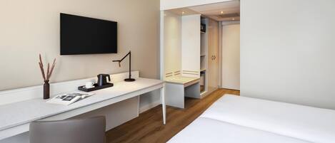 A modern hotel room with a white desk, a chair, a bed, and a wardrobe.