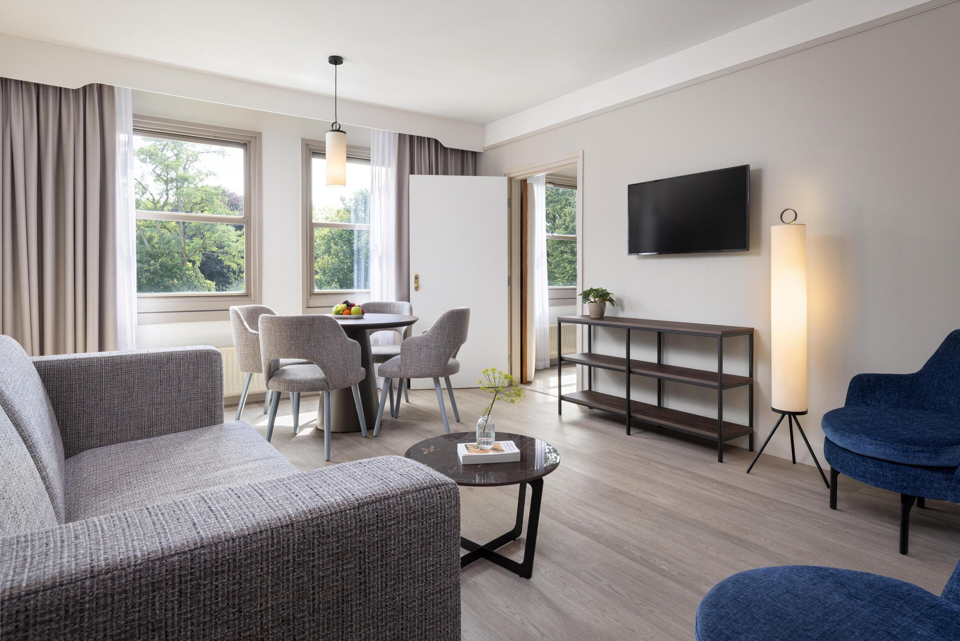 A modern living room with a sofa, chairs, a dining table, a TV, and a lamp.