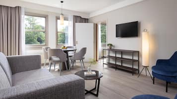 A modern living room with a sofa, chairs, a dining table, a TV, and a lamp.