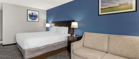 A hotel room with a bed, a nightstand with lamps, a couch, and two framed pictures on the walls.