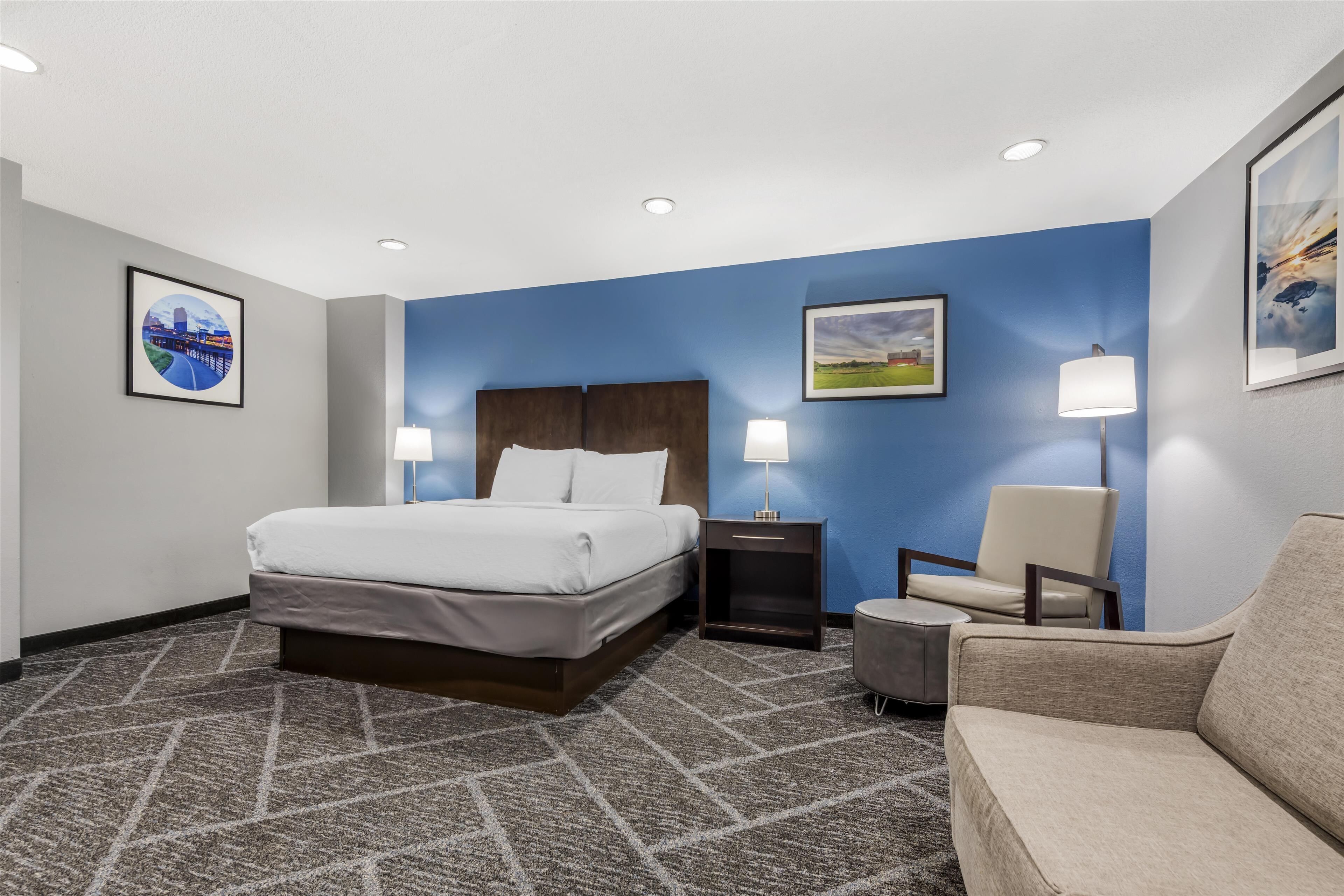 A hotel room with a large bed, a chair, a desk, and two wall-mounted lamps.