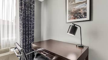A hotel room with a desk, chair, and a framed picture on the wall.