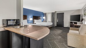 A hotel room with a kitchen area, a bed, a TV, and a seating area.