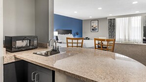 A modern kitchen with granite countertops, a built-in microwave, and a sink. There are two wooden chairs and a small table.
