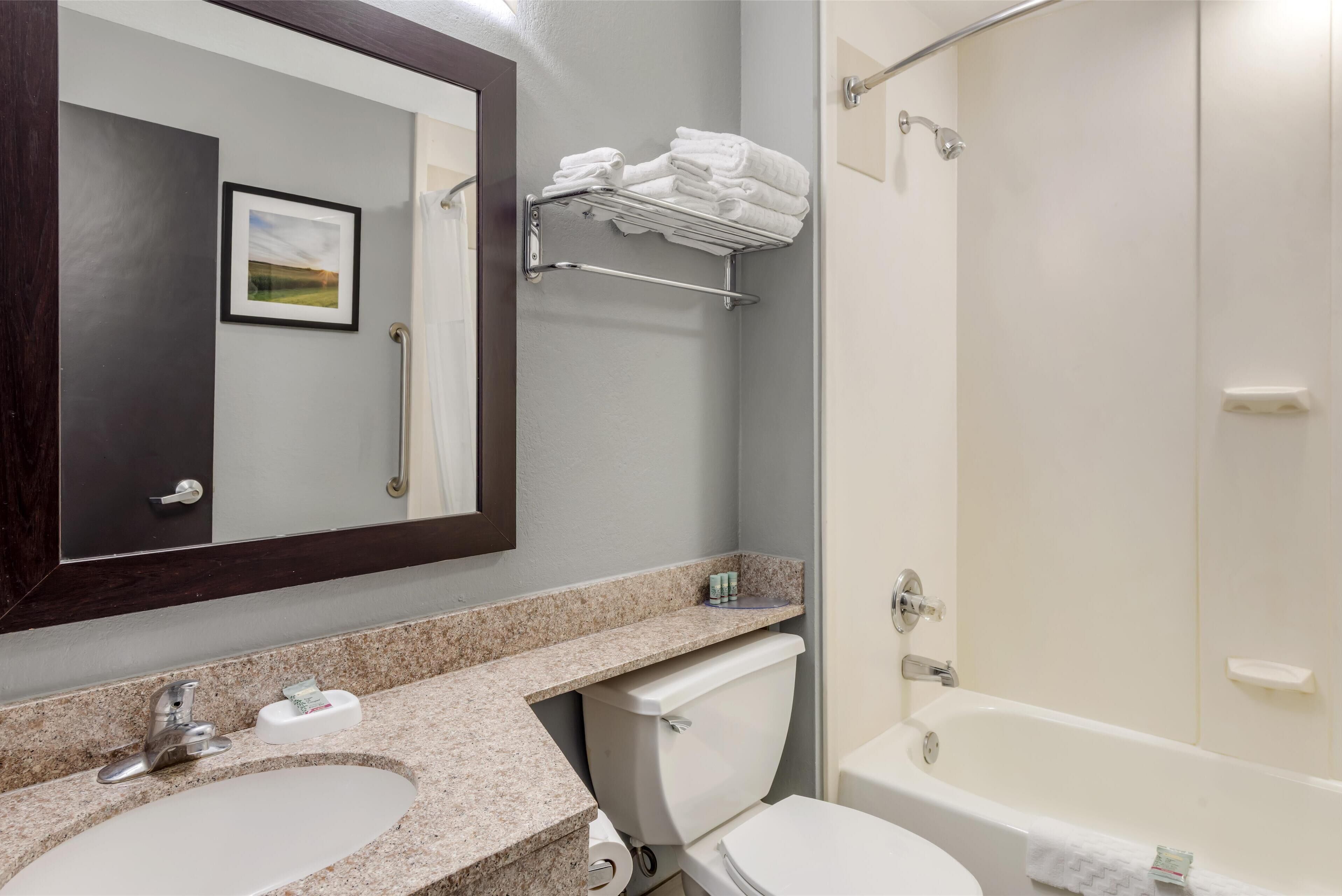 A bathroom with a sink, toilet, and bathtub. There is a towel rack above the toilet and a framed picture on the wall.