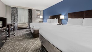 A hotel room with two beds, a desk with a chair, a TV, and a window with curtains.