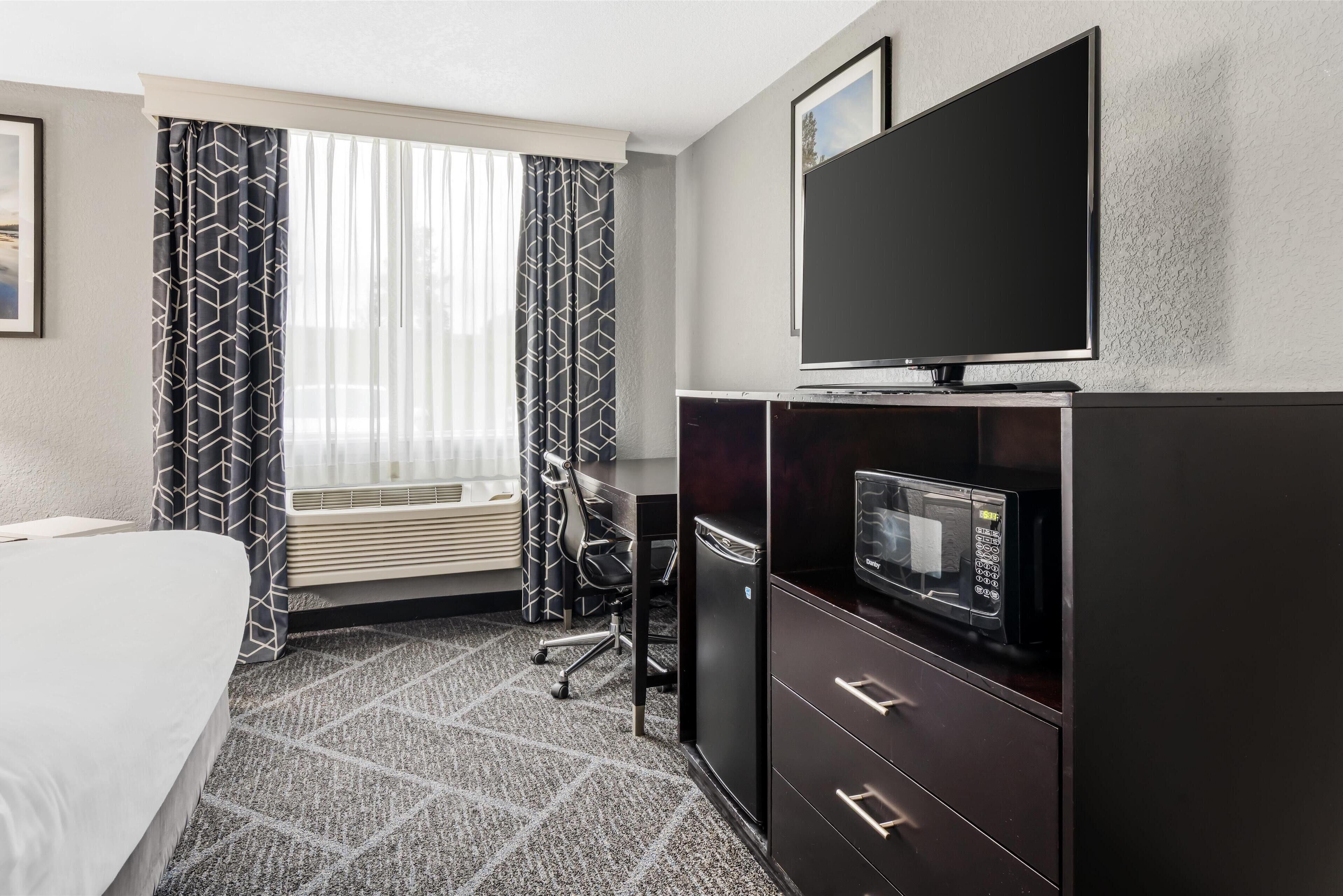 A hotel room with a bed, a desk with a chair, a television, and a microwave.