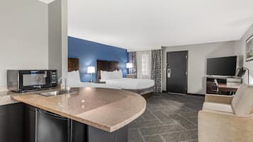 Habitación de hotel con cocina, cama, televisión y zona de estar.