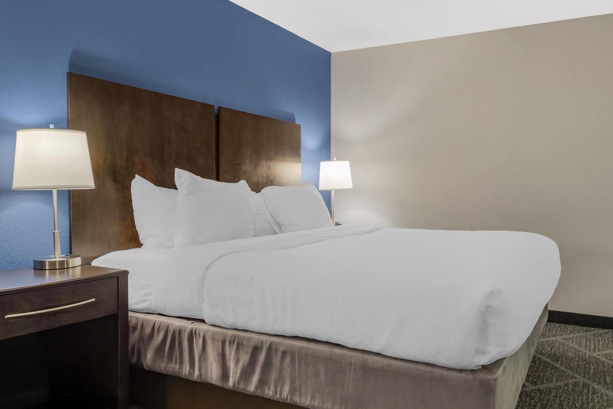 A neatly made bed with white linens, two bedside lamps, and a wooden headboard.