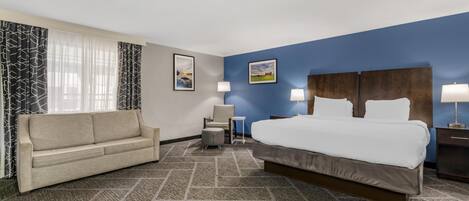 Habitación de hotel con una cama grande, un sofá, una silla, una mesita pequeña y dos lámparas de pared.