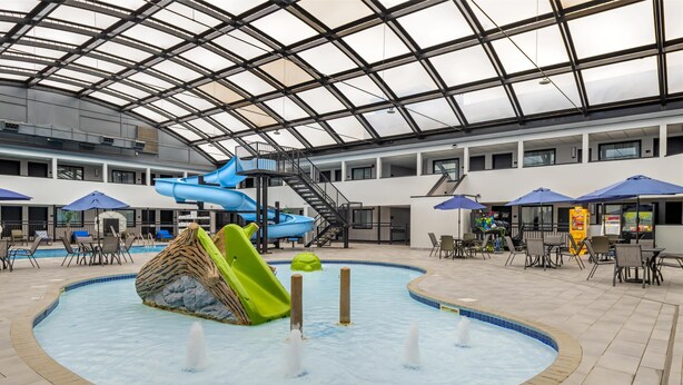 An indoor swimming pool with slides, seating areas, and a covered section with umbrellas.