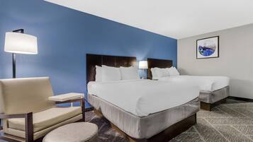 A hotel room with two beds, a chair, a lamp, and a framed picture on the wall.
