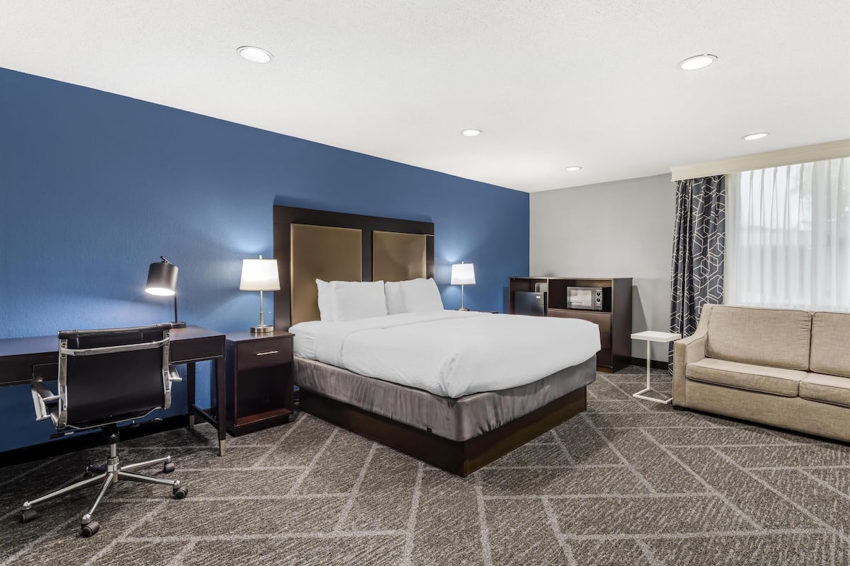 A hotel room with a large bed, a desk with a chair, a sofa, and a small table.