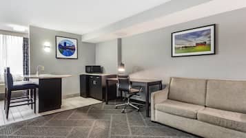 A modern hotel room with a kitchenette, a sofa, a desk, and two framed pictures on the wall.