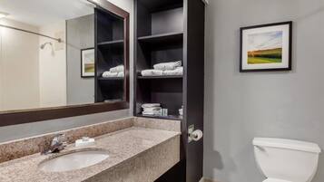 Une salle de bain avec un lavabo doté d’un plan de toilette en granit, un grand miroir, des toilettes et une étagère avec des serviettes pliées.