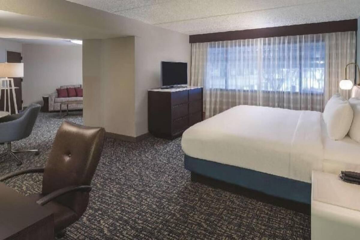 A hotel room with a bed, a desk, a chair, a TV, and a window with curtains.