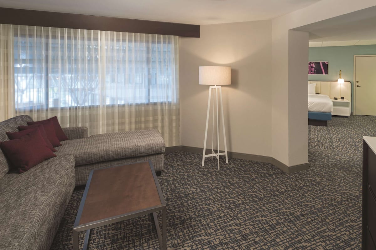 A hotel room with a sofa, a coffee table, a floor lamp, a bed, a desk, and a TV.