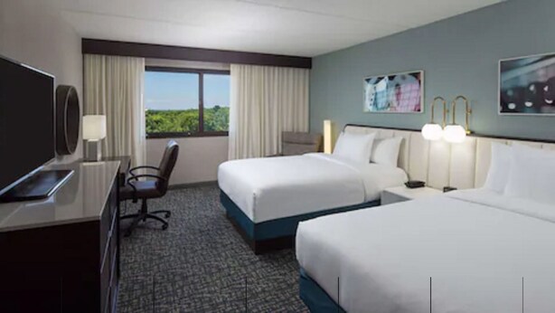 A hotel room with two beds, a desk with a flat-screen TV, a chair, and a window with curtains. - DoubleTree by Hilton Hotel Austin Northwest Arboretum (Austin)
