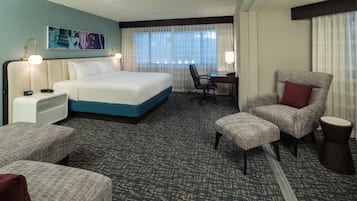 A hotel room with a bed, a desk, a chair, and a small table.
