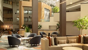 A spacious lobby with a high ceiling, multiple seating areas, and a central plant. - DoubleTree by Hilton Hotel Austin Northwest Arboretum (Austin)