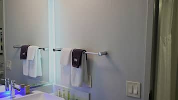 A bathroom with a white sink, mirror, and towel rack. There are two towels hanging on the rack, one white and one with a dark towel head.