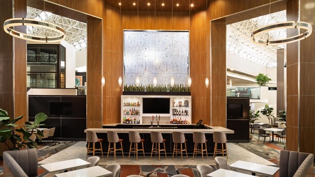A modern bar area with a central island, bar stools, and seating arrangements. - DoubleTree by Hilton Hotel Austin Northwest Arboretum (Austin)