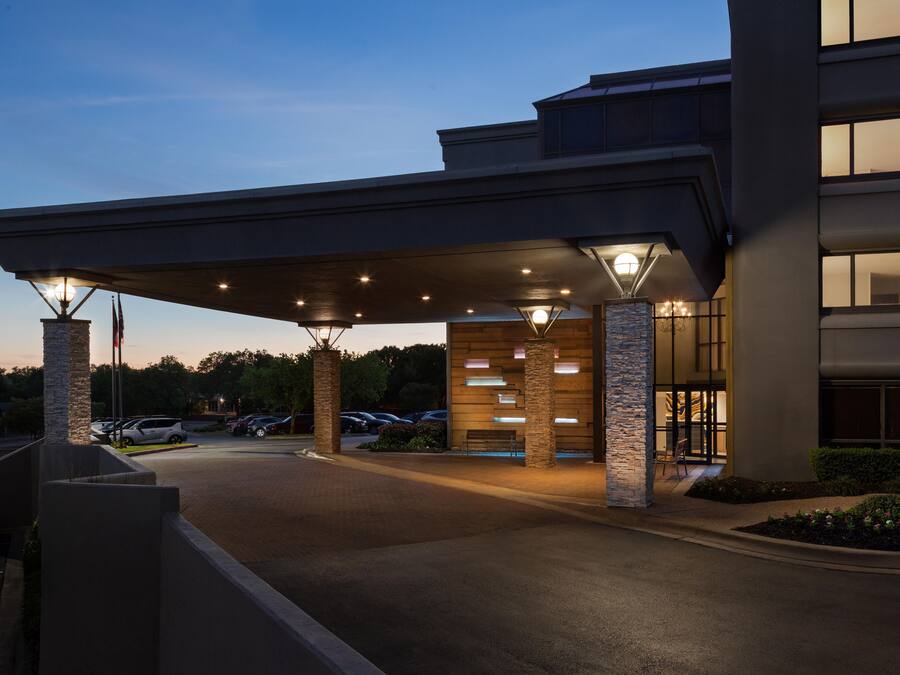 Ein Hotel mit Eingangsbereich, überdachtem Gang, Steinsäulen und einem Parkplatz.