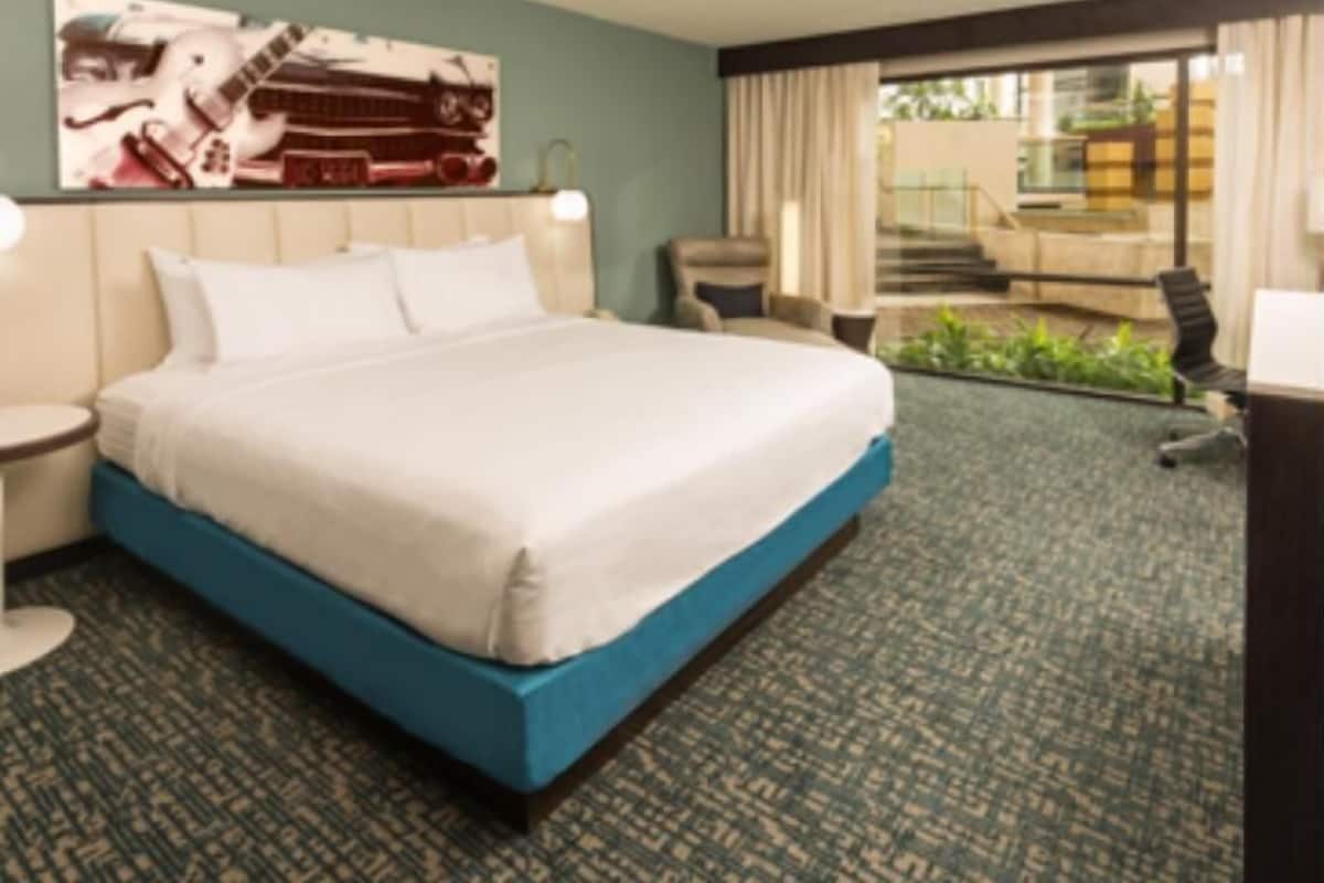 A hotel room with a large bed, a desk, a chair, a window with a view of a building, and a staircase.