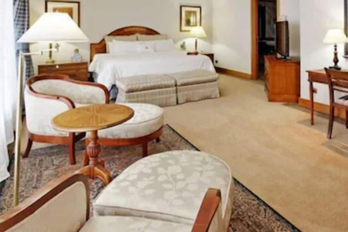 Una habitación de hotel con cama, dos sillas, escritorio y televisor.