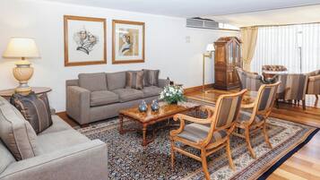 Un salon comprenant un canapé, des fauteuils, une table basse et un tapis. Deux œuvres d’art encadrées ornent le mur, ainsi qu’un meuble en bois.