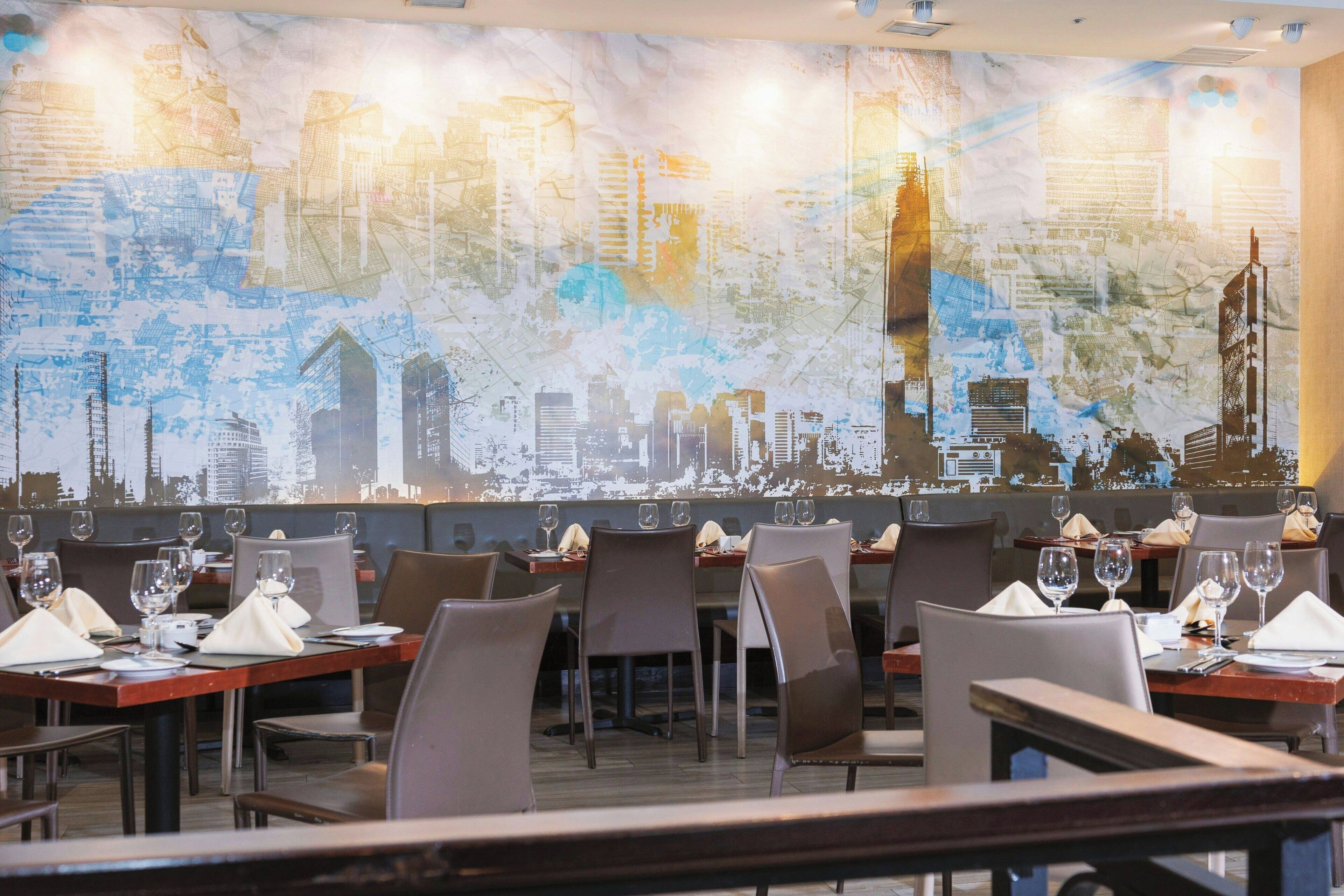 A restaurant with tables set for dining, featuring a cityscape mural on the wall.