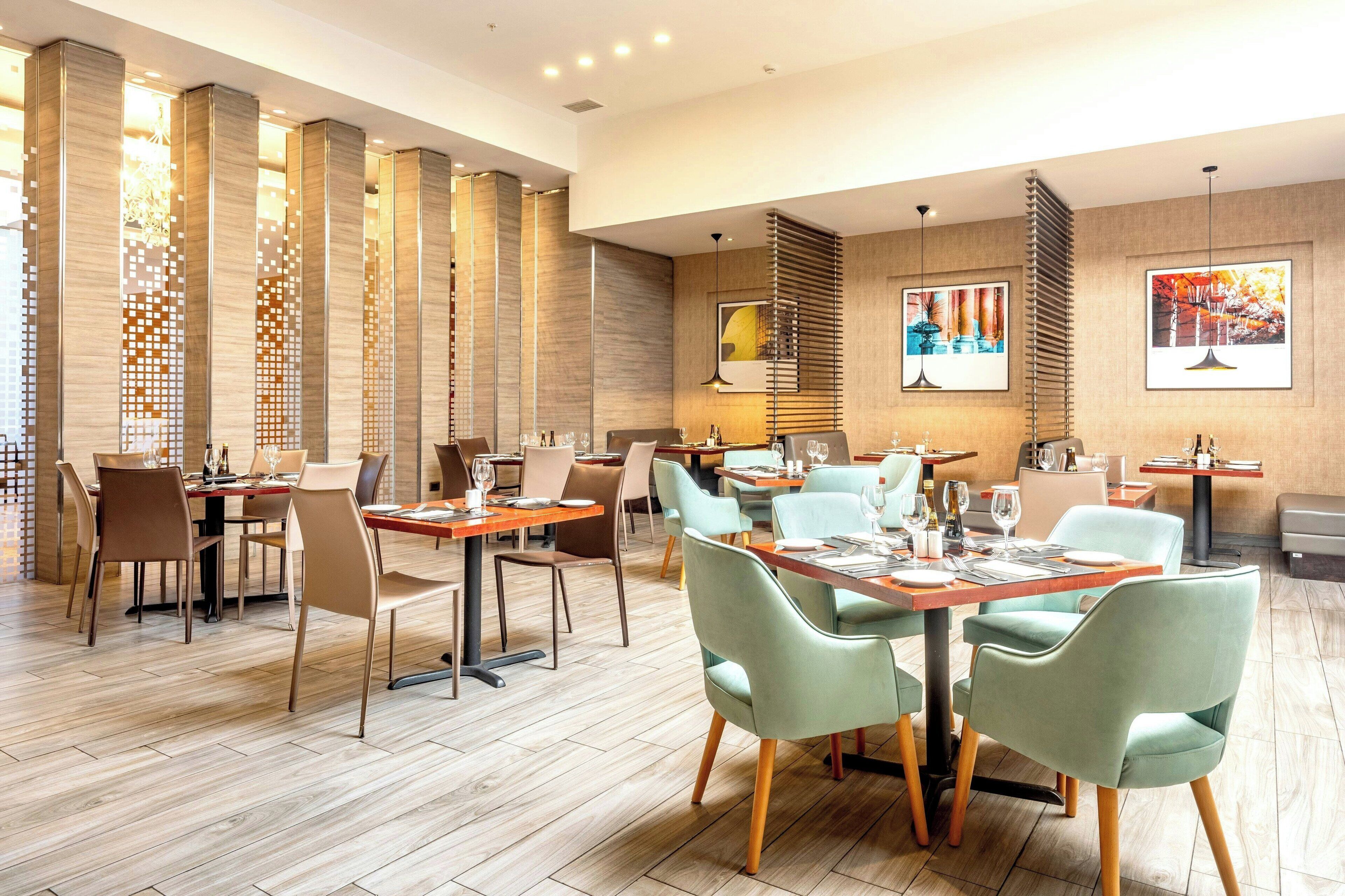 Un restaurante moderno con pisos de madera, sillas verdes y marrones, y mesas dispuestas para comer.