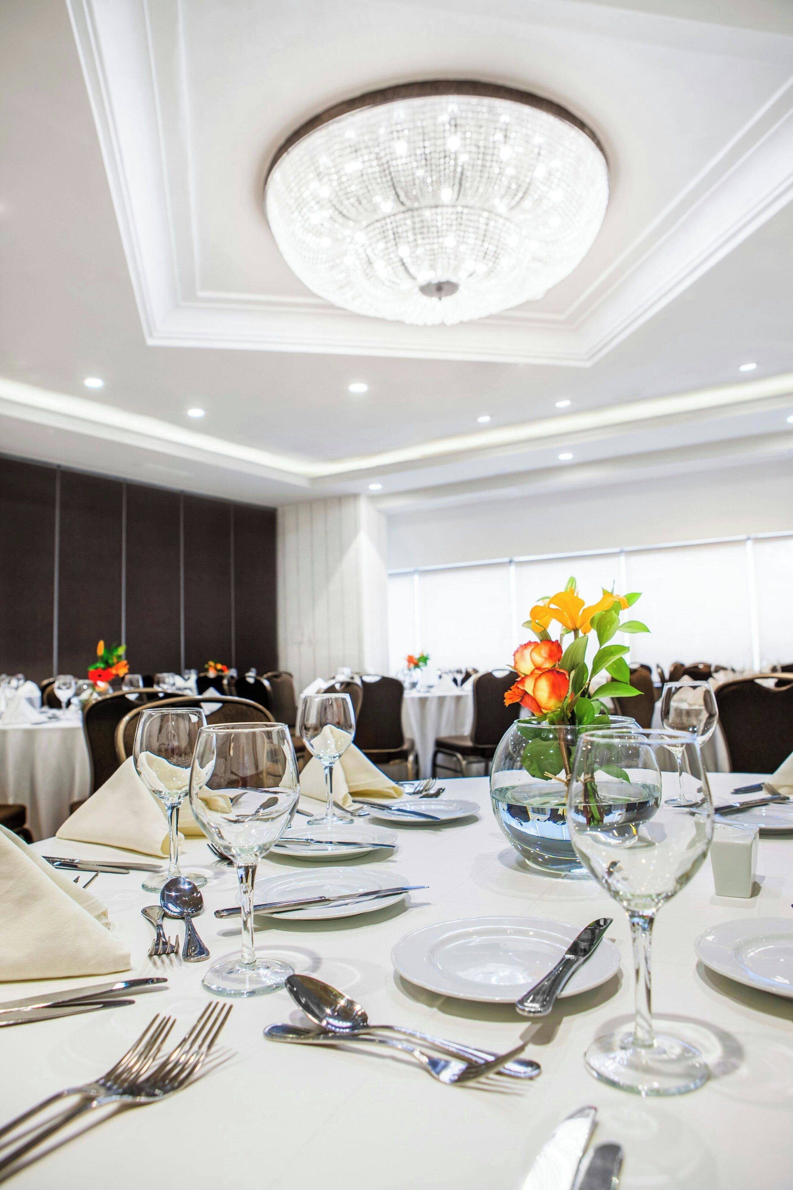 A dining area with tables set for a formal meal, featuring crystal chandeliers and floral centerpieces.