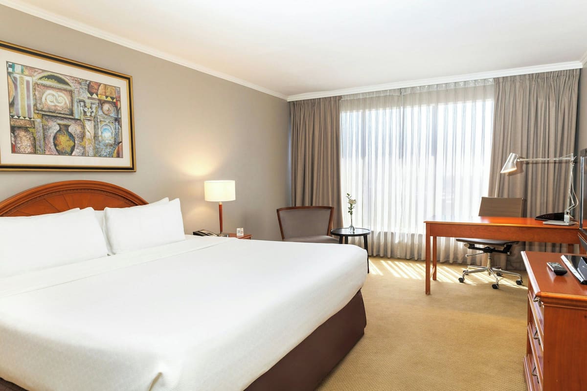 Habitación de hotel con una cama grande, un escritorio, una silla, una lámpara y un cuadro en la pared.