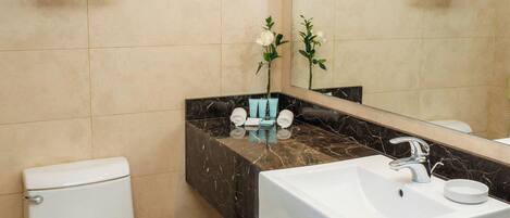 Un baño moderno con inodoro blanco, lavabo de mármol y un espejo grande.
