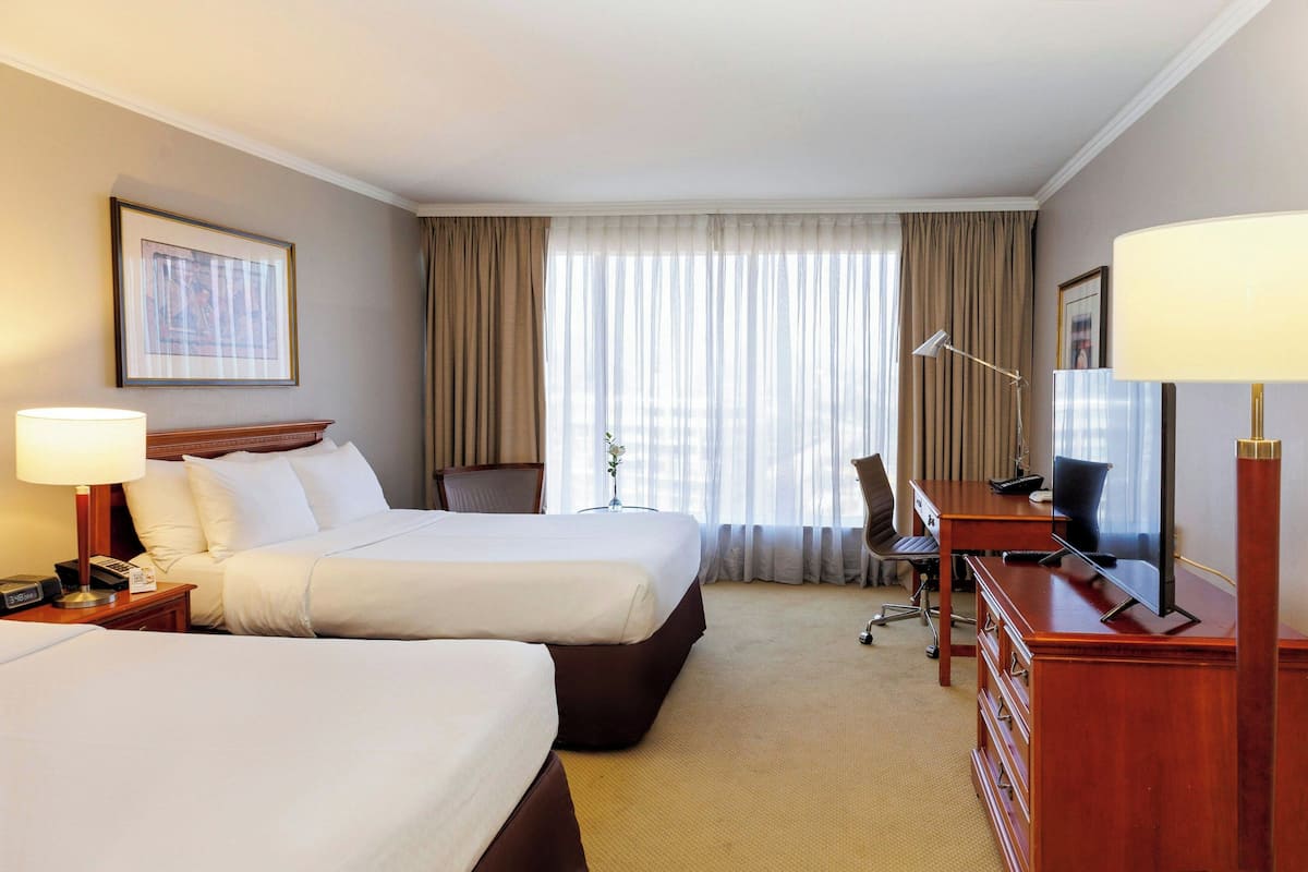Habitación de hotel con dos camas, un escritorio con computadora, una lámpara y un televisor.