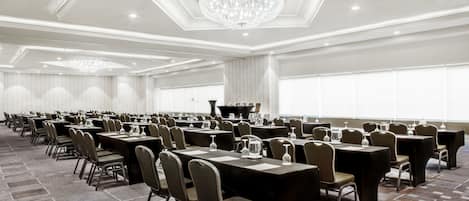 A large conference room with rows of tables and chairs, a chandelier, and a stage with a piano.