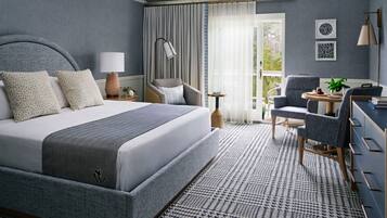 A modern hotel room with a large bed, a desk, a chair, and a balcony with curtains.