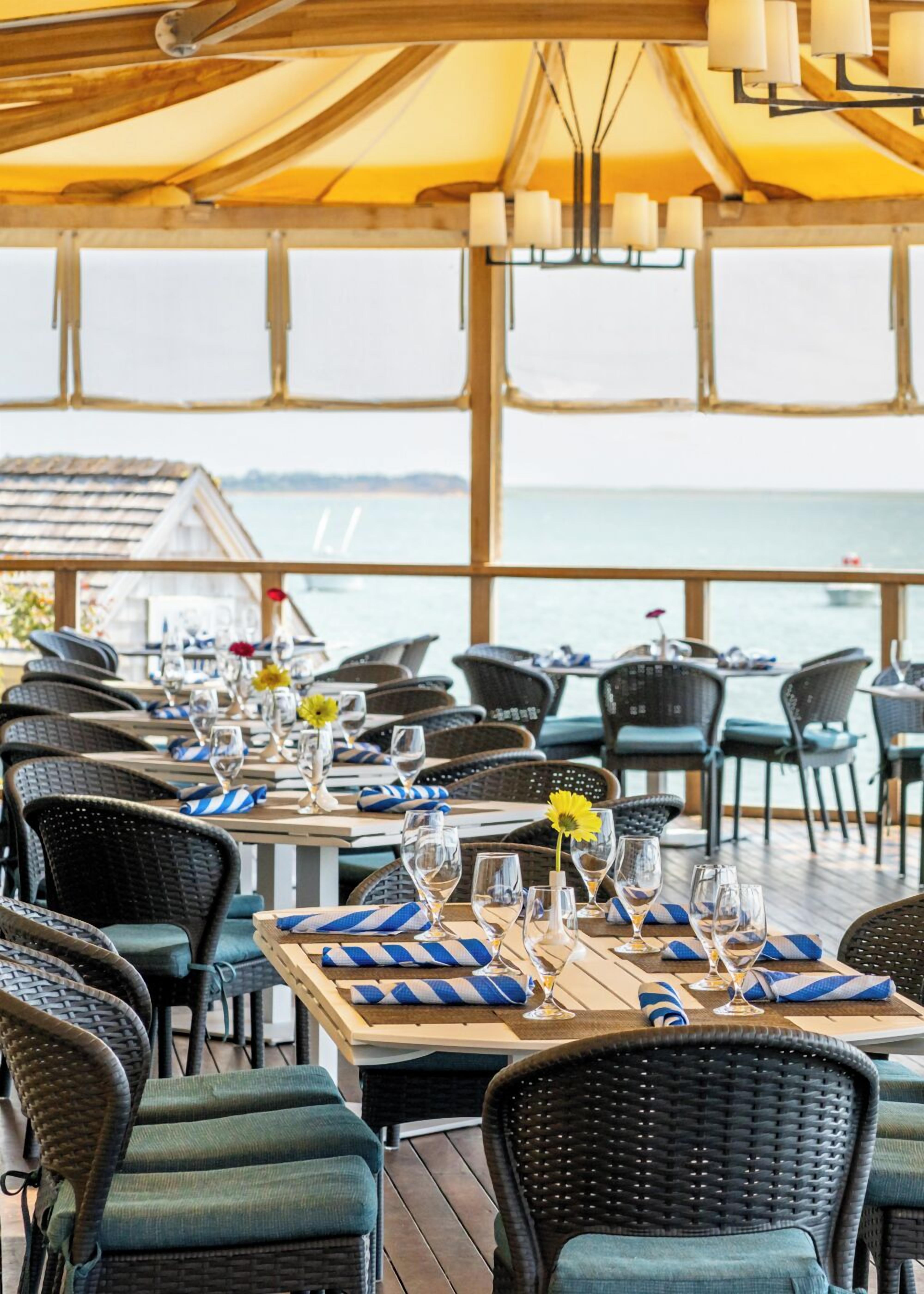 An outdoor dining area with wicker chairs and tables, set against a view of the sea.