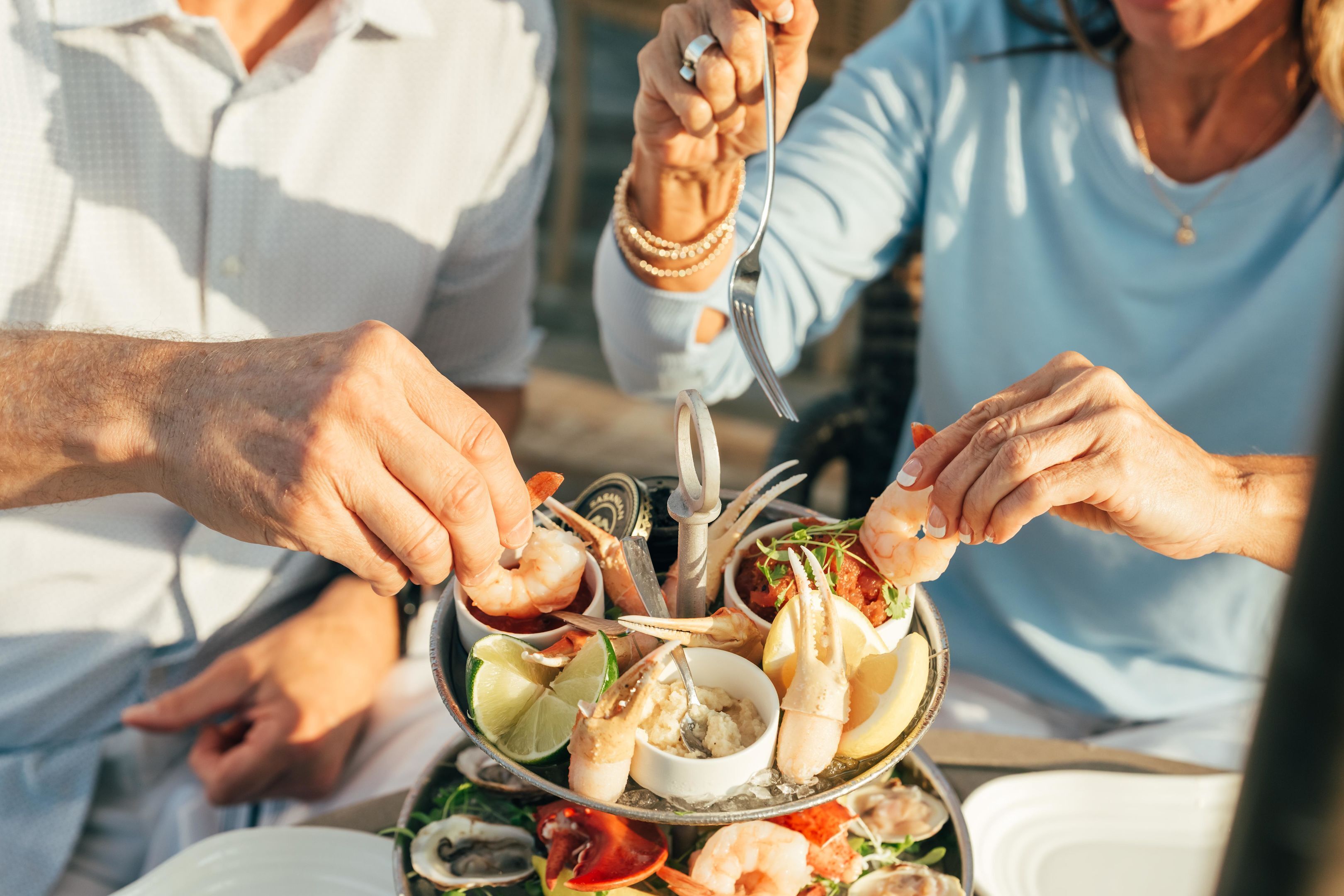 Um grupo de pessoas jantando em uma mesa ao ar livre, com uma travessa de frutos do mar.