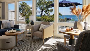 A sunlit room with a view of the sea, featuring a sofa, a round table, and a chair. - Wequassett Resort and Golf Club (Harwich)