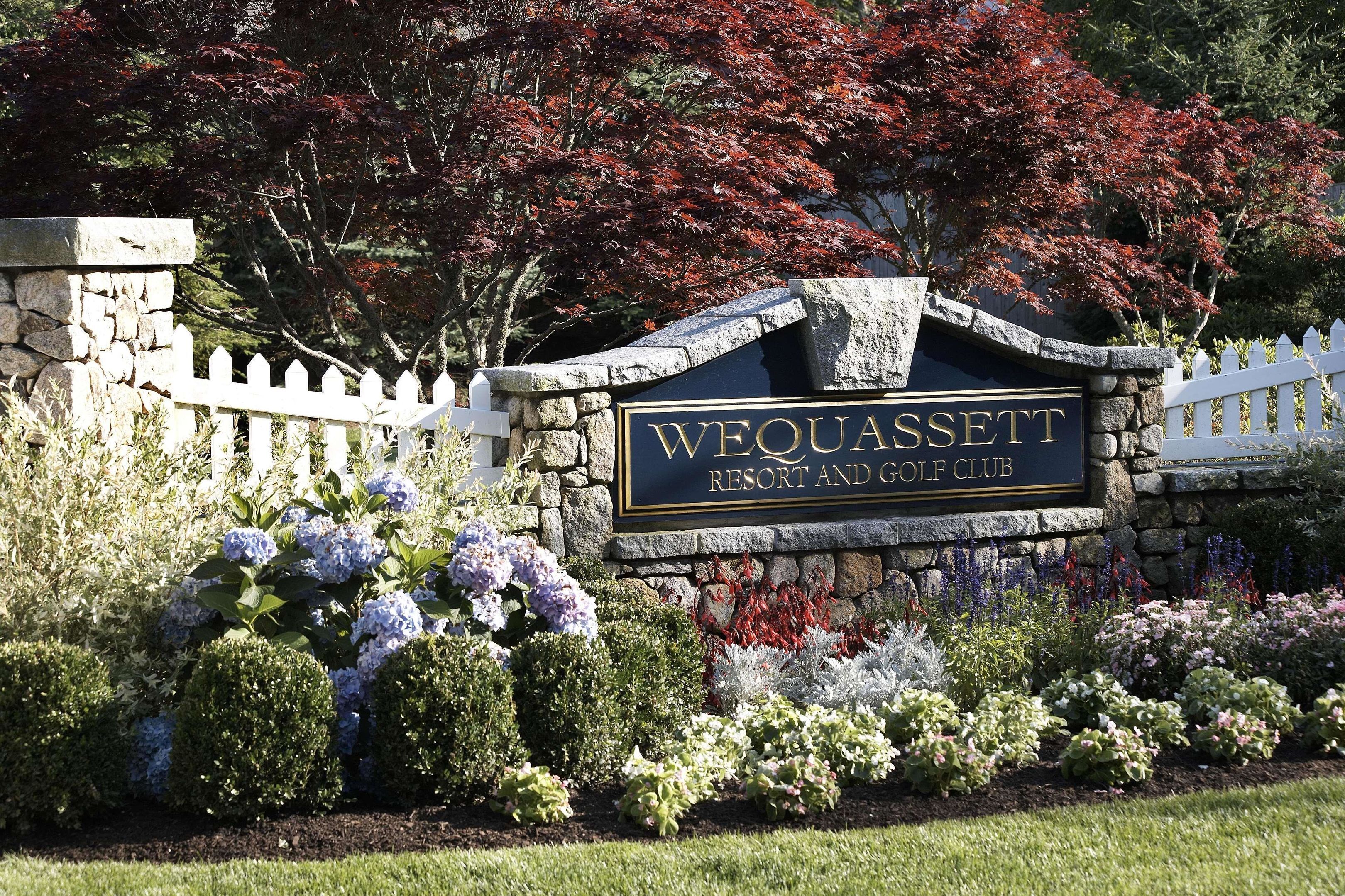 A sign for Wequassee Resort and Golf Club with a stone wall and white picket fence.
