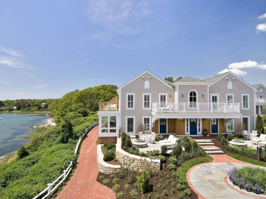 A large two-story house with a balcony, a stone pathway, and a view of a lake.