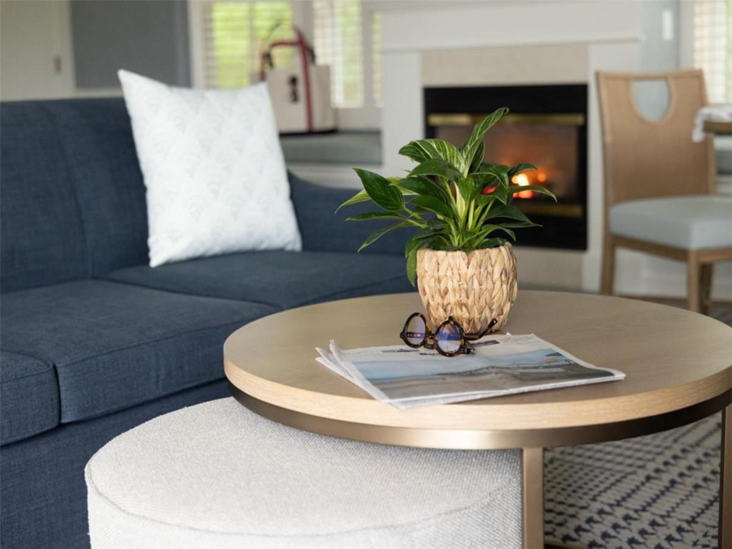 Un salon avec un canapé, une table basse ronde sur laquelle se trouvent un magazine et des verres, et une plante dans un pot en fibres tressées.